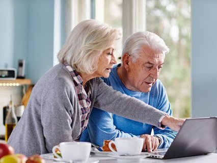 Zwei ältere Personen sitzen am Tisch und schauen auf einem Laptop