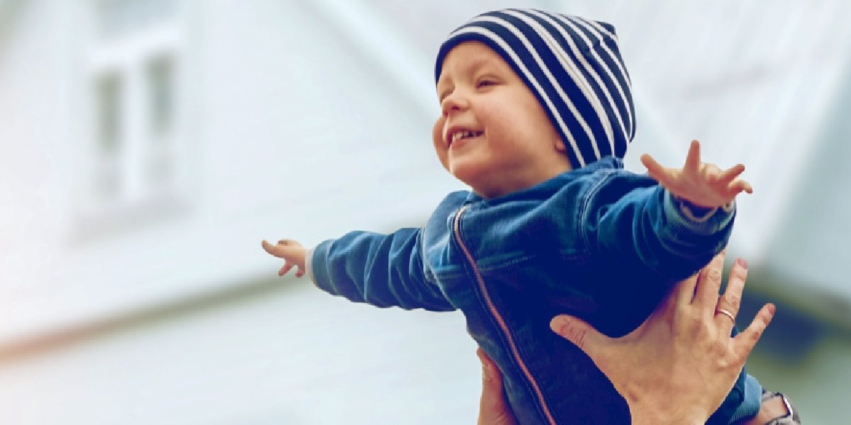 Vergnügtes Kind wird vor Haus in der Luft gehalten
