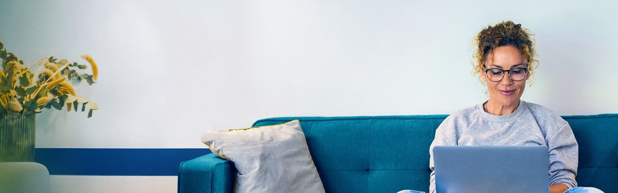 Beispielbild junge Frau recherchiert am Laptop auf einem Sofa