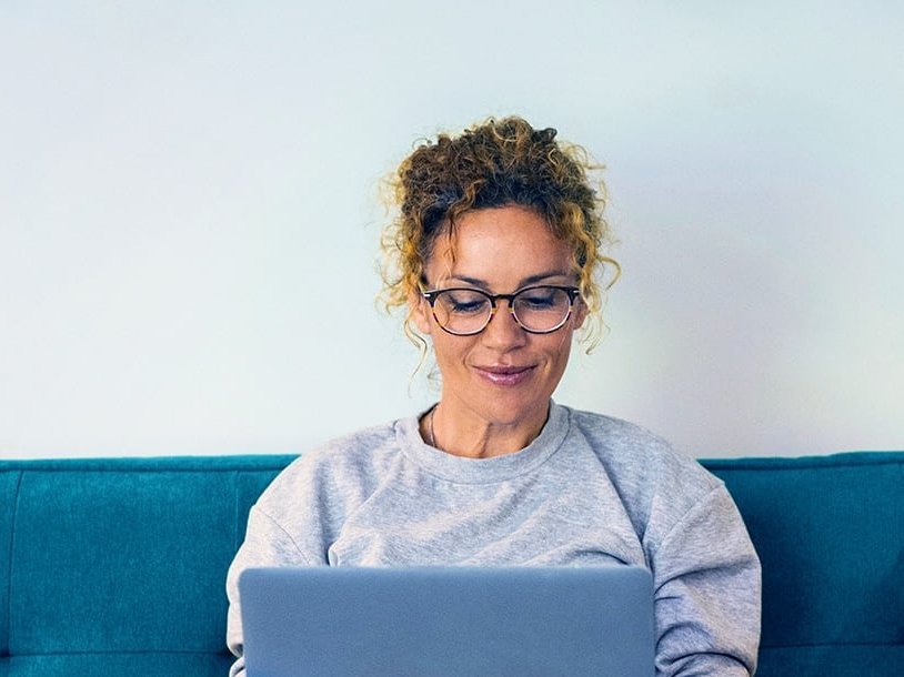 Beispielbild junge Frau recherchiert am Laptop auf einem Sofa