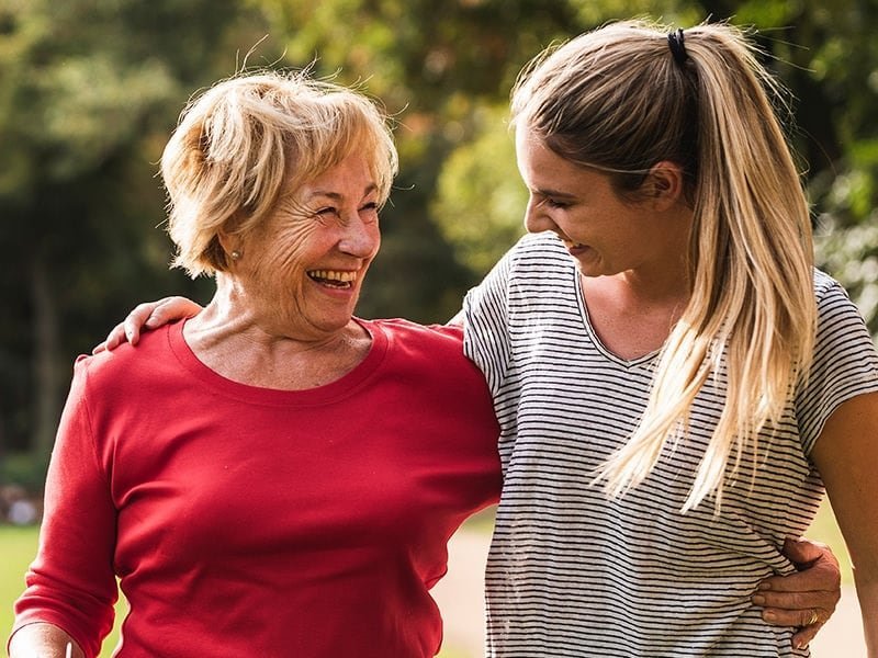 Ältere Frau und jüngere Frau, Arm in Arm, glücklich auf einer sonnigen Wiese