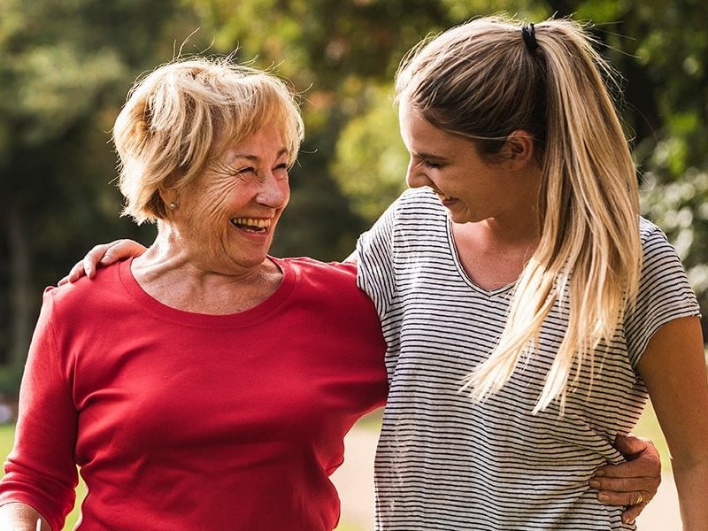 Ältere Frau und jüngere Frau, Arm in Arm, glücklich auf einer sonnigen Wiese