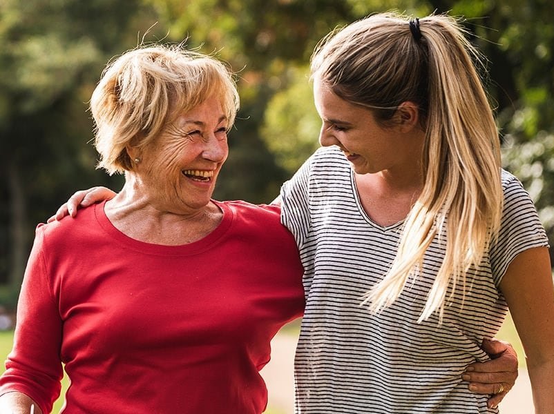 Ältere Frau und jüngere Frau, Arm in Arm, glücklich auf einer sonnigen Wiese