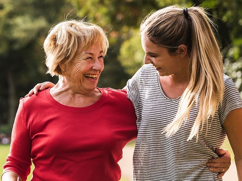 Ältere Frau und jüngere Frau, Arm in Arm, glücklich auf einer sonnigen Wiese