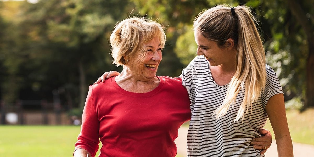 Ältere Frau und jüngere Frau, Arm in Arm, glücklich auf einer sonnigen Wiese